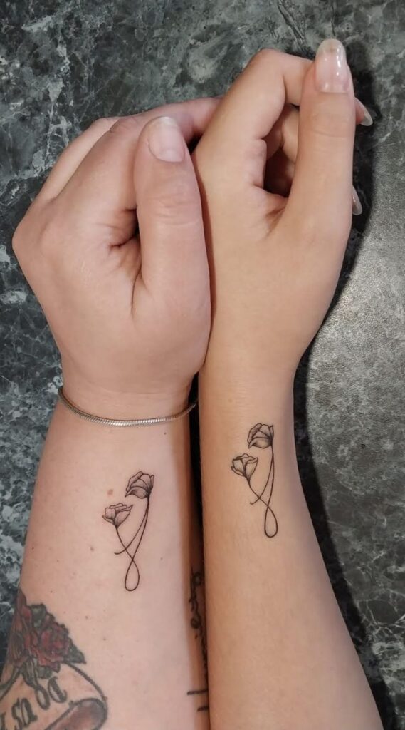 Mom and daughter Tattoo🥰 Matching minimalist floral tattoos on forearms with interlocking stems, symbolizing connection and unity. | Sky Rye Design Matching minimalist floral tattoos on forearms with interlocking stems, symbolizing connection and unity.