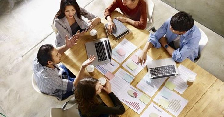 Most small business owners lack a succession plan Team collaboration at a desk with laptops and charts, discussing business strategy over coffee in a bright office space. | Sky Rye Design Team collaboration at a desk with laptops and charts, discussing business strategy over coffee in a bright office space.