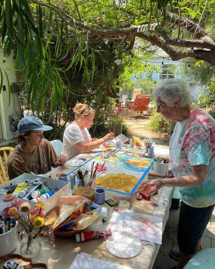 Group of people enjoying an outdoor art session, painting and crafting under a leafy pergola with vibrant colors and natural light.