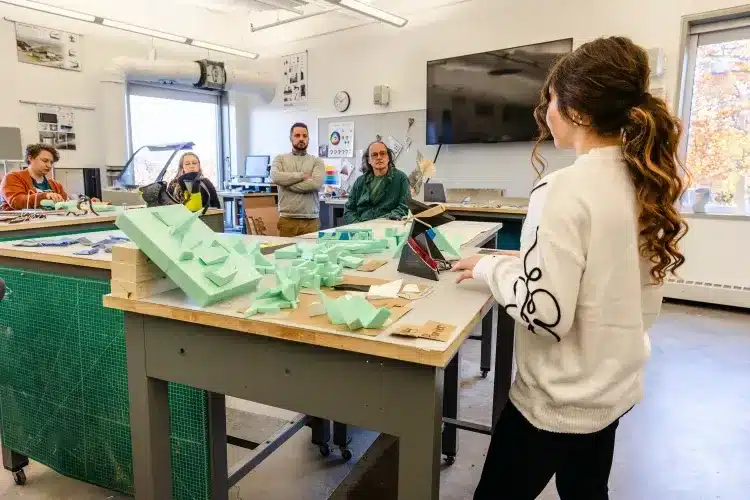 NMU62431-Enhanced-NR-231030-AD-Day-1-HCD_0jpgwebp Student presenting architectural model to classmates in a design studio, discussing concepts and receiving feedback during a classroom session. | Sky Rye Design Student presenting architectural model to classmates in a design studio, discussing concepts and receiving feedback during a classroom session.