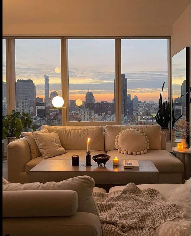 New York City has my heart Cozy modern living room with candles and city skyline view at sunset through large windows, featuring plush sofas and elegant decor. | Sky Rye Design Cozy modern living room with candles and city skyline view at sunset through large windows, featuring plush sofas and elegant decor.
