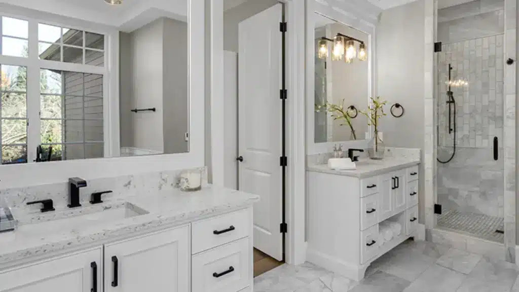 Elegant bathroom with white granite countertops, modern fixtures, double vanity, large mirrors, and a sleek glass shower enclosure.