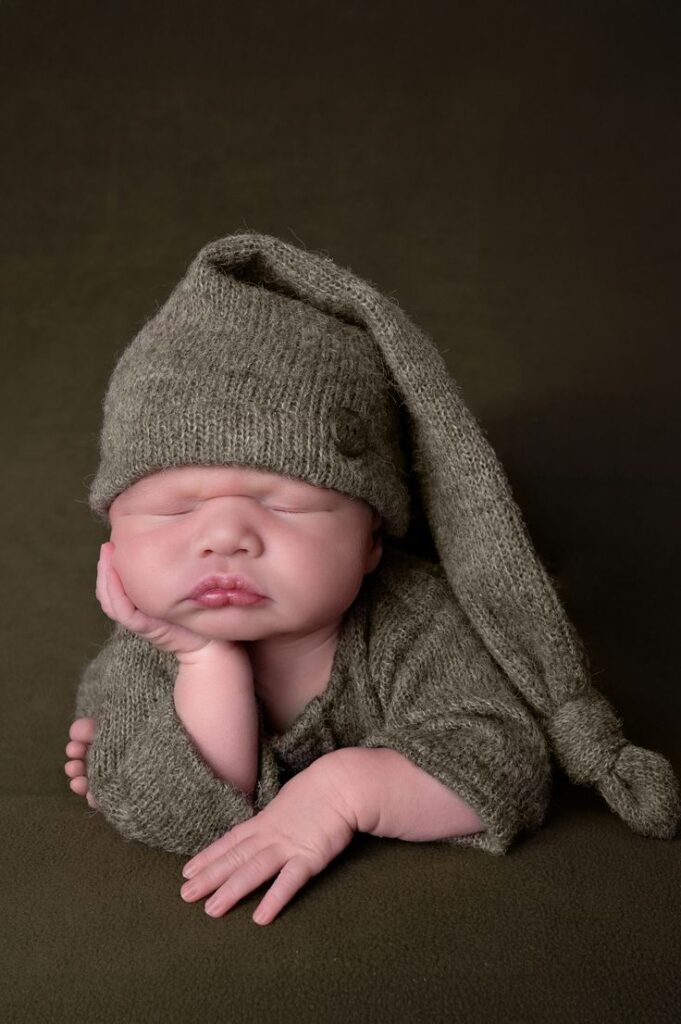 Newborn Photoshoot Pretoria Classic Froggy Pose with Cozy Green Outfit Sleeping newborn baby wearing a knitted green hat and outfit, posed with head resting on hand, against a cozy dark background. | Sky Rye Design Sleeping newborn baby wearing a knitted green hat and outfit, posed with head resting on hand, against a cozy dark background.