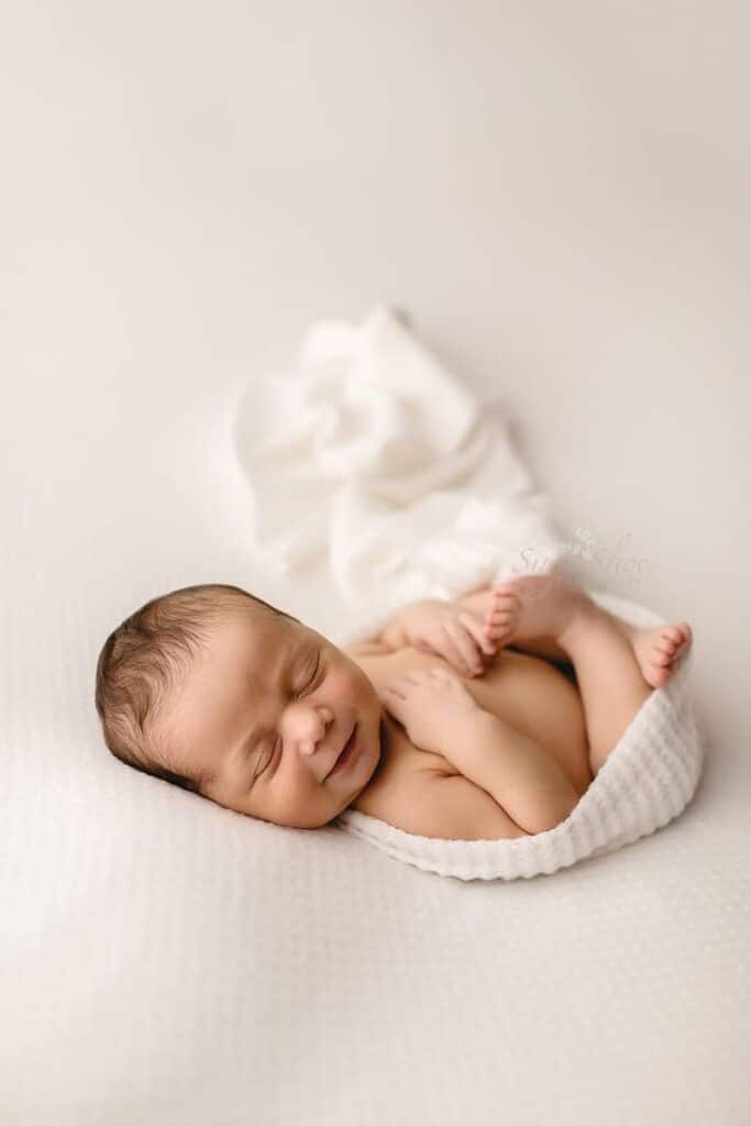 Newborn pose baby sleeping on back with arms and legs folded wrapped in white wrap smiling Sleeping newborn baby wrapped in white blanket on soft bed, peaceful and serene. | Sky Rye Design Sleeping newborn baby wrapped in white blanket on soft bed, peaceful and serene.