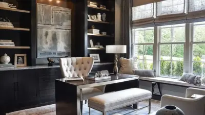 Stylish home office with dark wood shelves, modern desk, tufted chair, large window, and cozy seating, bathed in natural light.