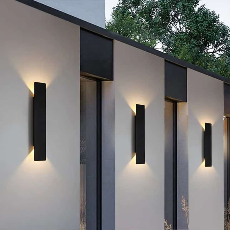 Modern outdoor wall lights illuminating a building facade during evening, enhancing architectural design with sleek, vertical fixtures.