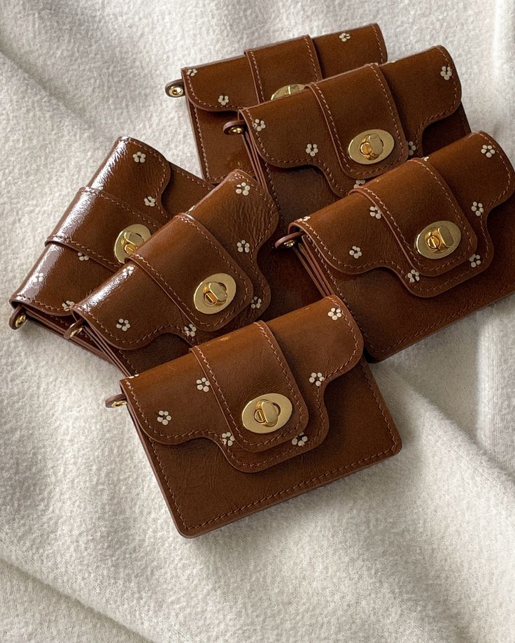 Brown floral leather wallets with gold clasps arranged on a soft white fabric background, showcasing elegant and stylish design.