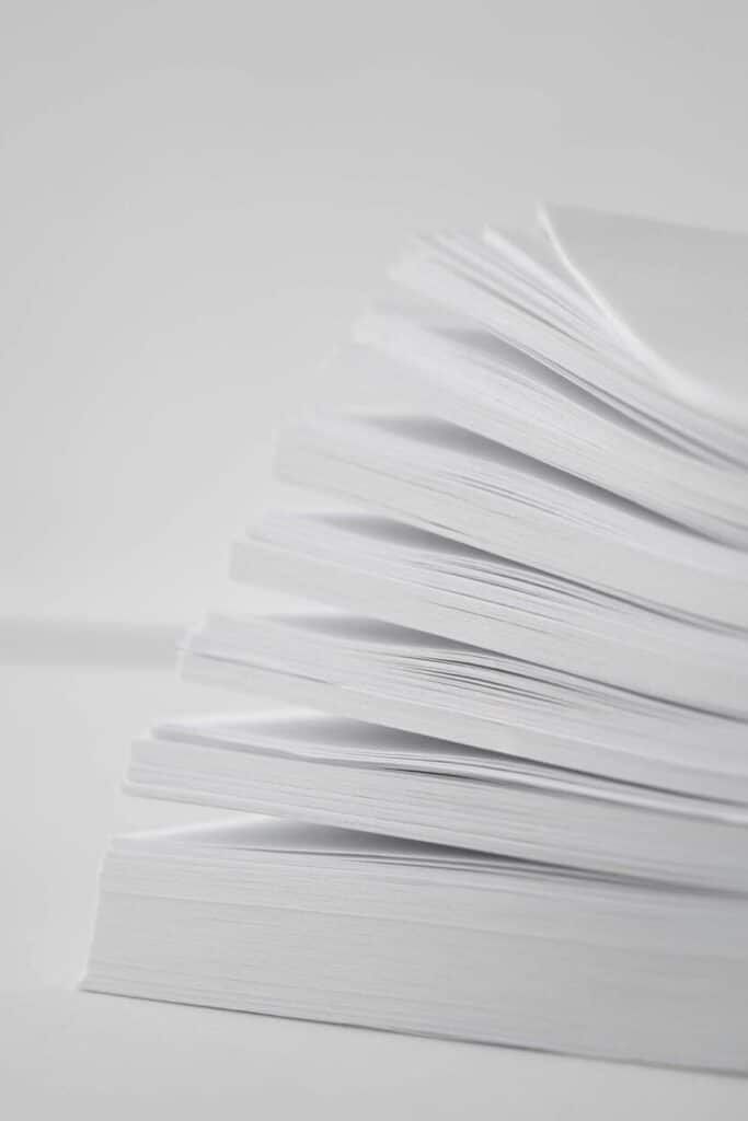 Stack of white paper sheets arranged neatly, viewed from the side, highlighting texture and simplicity in a minimalistic setting.