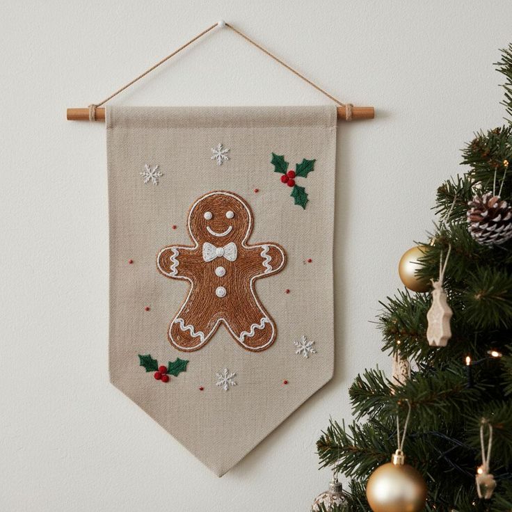 Personalized Christmas Banner with Gingerbread Embroidery Holiday Hand Embroidered Linen Flag Christmas Decor Handmade Christmas Gift Festive wall banner with a smiling gingerbread man, snowflakes, and holly beside a decorated Christmas tree with golden ornaments. | Sky Rye Design Festive wall banner with a smiling gingerbread man, snowflakes, and holly beside a decorated Christmas tree with golden ornaments.