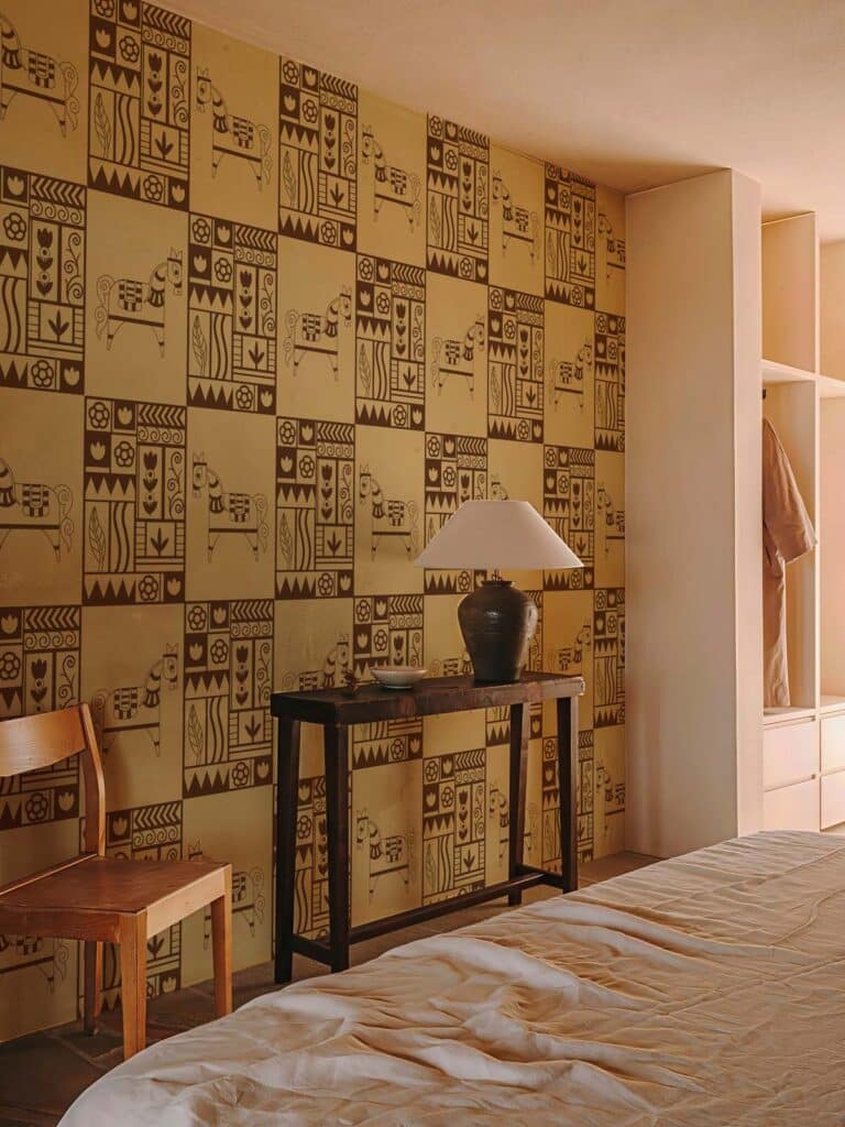 Petroglyphs-Warm-Brown-Tribal-Pattern-Wallpaper-M Cozy bedroom with patterned wallpaper, wooden furniture, and soft lighting. Ideal blend of modern and rustic decor elements. | Sky Rye Design Cozy bedroom with patterned wallpaper, wooden furniture, and soft lighting. Ideal blend of modern and rustic decor elements.