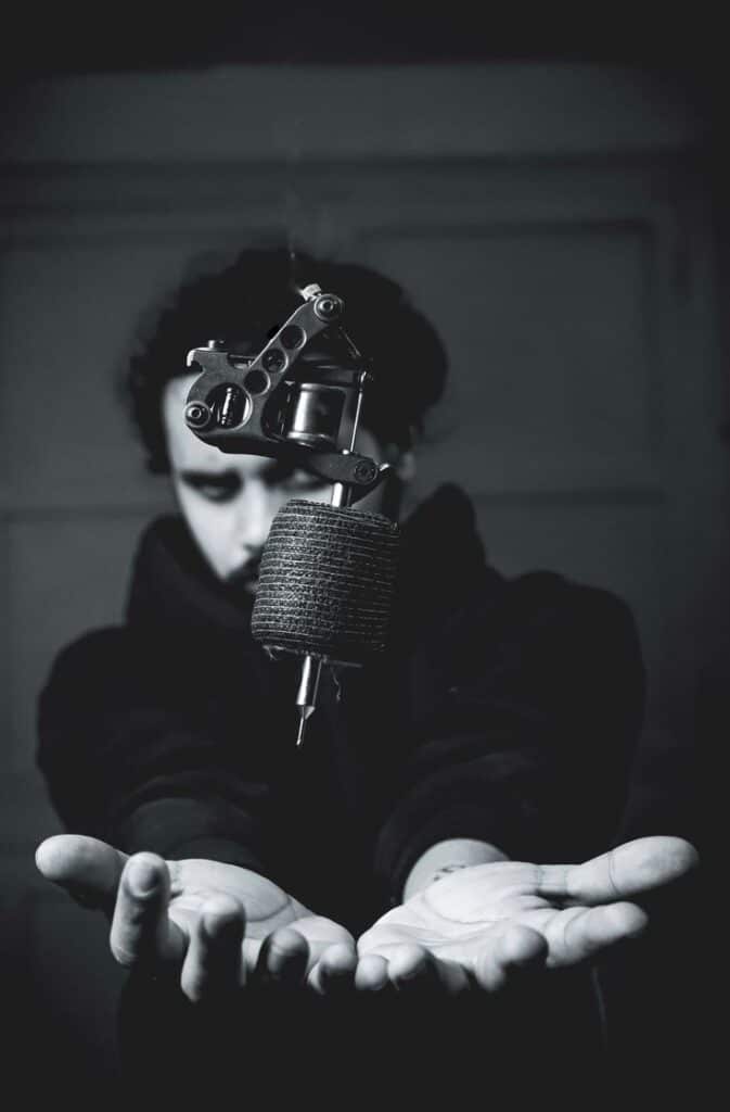 Photography Tattoo artist holding a tattoo machine with focus on the equipment, monochrome style, emphasizing creativity and craftsmanship. | Sky Rye Design Tattoo artist holding a tattoo machine with focus on the equipment, monochrome style, emphasizing creativity and craftsmanship.