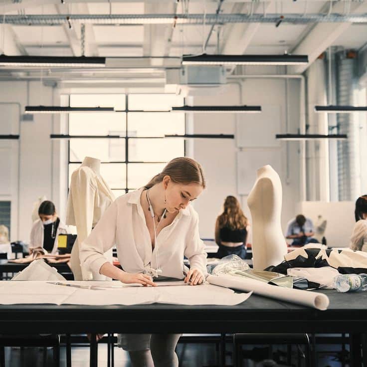 Quali sono le professioni e i corsi di moda più interessanti oggi_ Fashion design student focused on creating patterns in a bright workspace with mannequins and materials. | Sky Rye Design Fashion design student focused on creating patterns in a bright workspace with mannequins and materials.