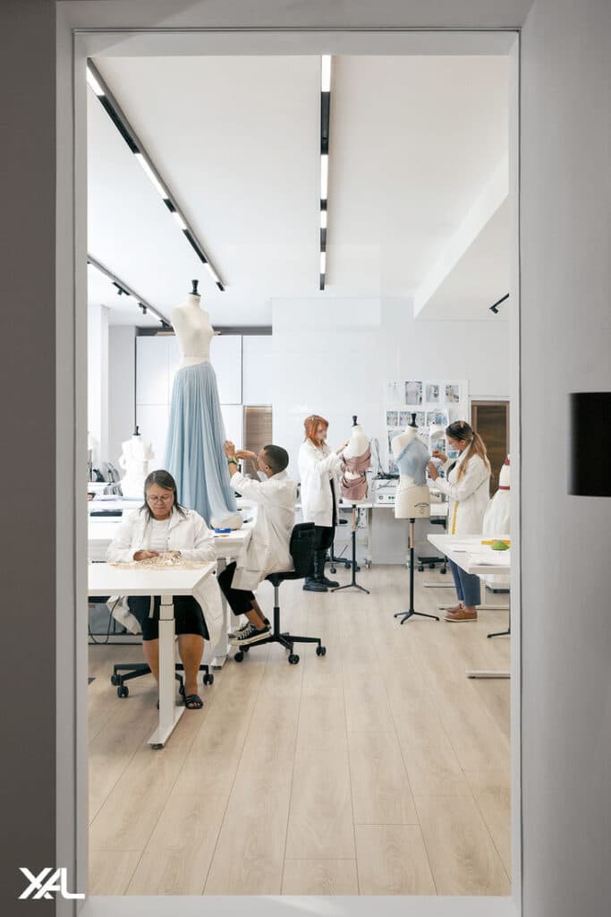 Fashion design students working on dressmaking in a modern studio with mannequins, sewing tables, and pattern sketches.