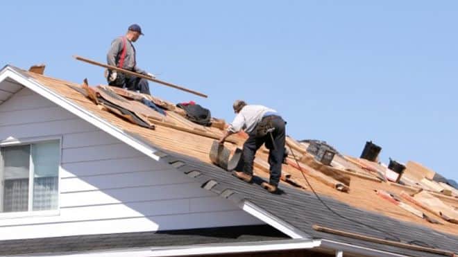 Roofers working on a house roof under blue sky, installing shingles for home improvement and roof repair.
