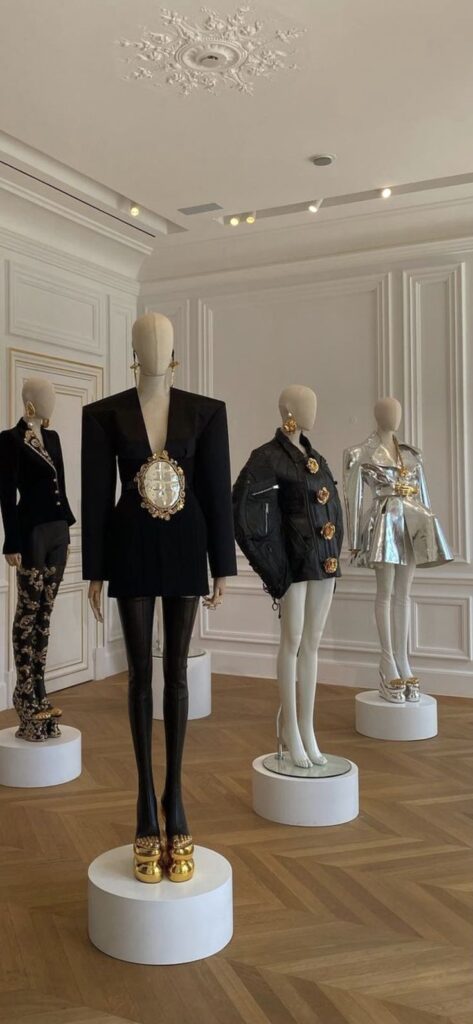 Schiaparelli Atelier _ Paris July 21 Mannequins display avant-garde fashion in a stylish showroom with ornate ceiling, featuring bold designs and metallic accents. | Sky Rye Design Mannequins display avant-garde fashion in a stylish showroom with ornate ceiling, featuring bold designs and metallic accents.