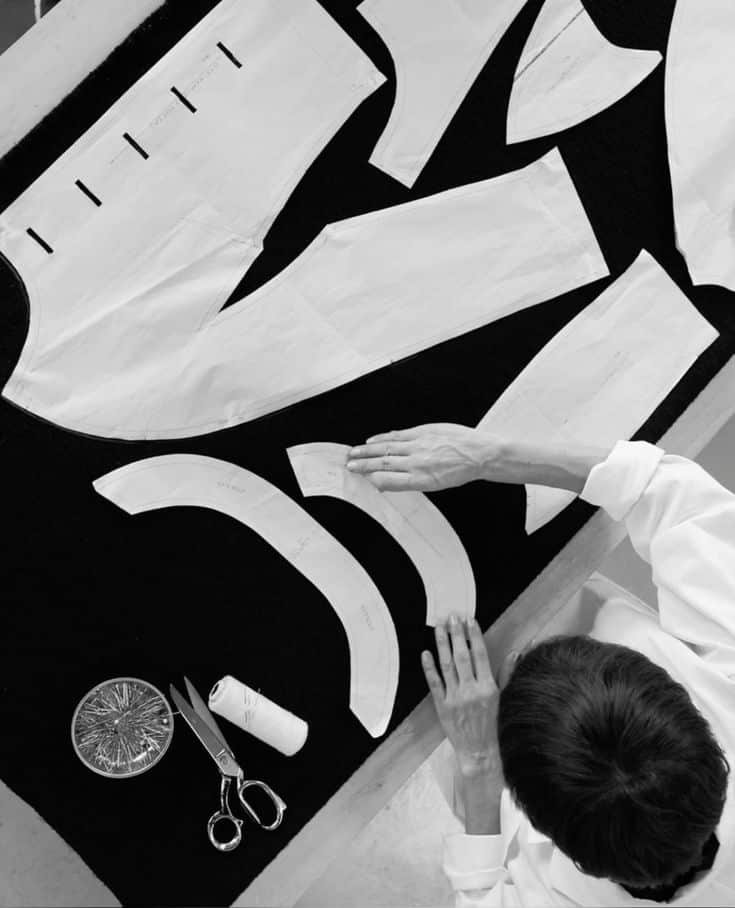 Seamstress birdseye view Person arranging garment patterns on black fabric with scissors, thread, and pins nearby, viewed from above. | Sky Rye Design Person arranging garment patterns on black fabric with scissors, thread, and pins nearby, viewed from above.