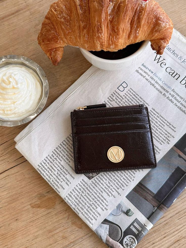 Croissant, coffee, and wallet on a newspaper-mat dining arrangement, perfect for a cozy morning breakfast setting.