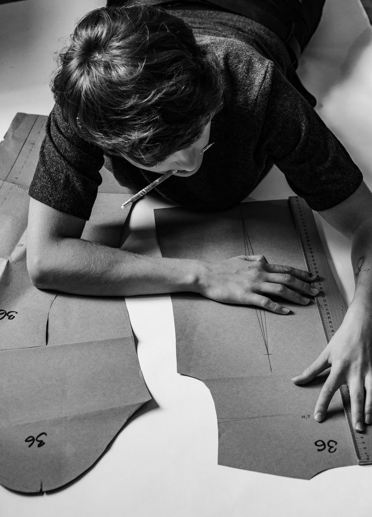 Sewing pattern maker 🪡 Person designing clothing patterns on paper, lying on the floor with a pencil in mouth, focusing on accurate measurements. Black and white image. | Sky Rye Design Person designing clothing patterns on paper, lying on the floor with a pencil in mouth, focusing on accurate measurements. Black and white image.