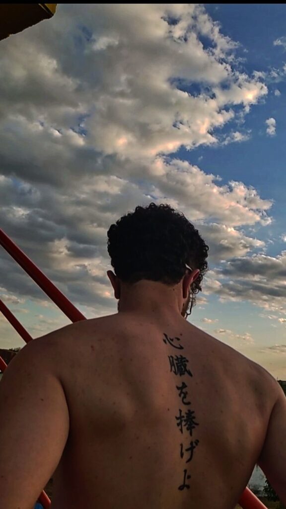 Man with Japanese tattoo on back looks at cloudy sky, showcasing body art and nature.