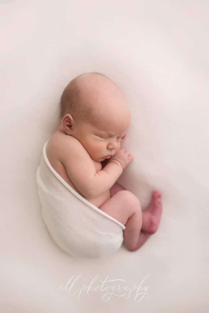 Side laying Sleeping newborn wrapped in white blanket on soft surface, showcasing peaceful sleeping pose. Perfect for baby photography themes. | Sky Rye Design Sleeping newborn wrapped in white blanket on soft surface, showcasing peaceful sleeping pose. Perfect for baby photography themes.