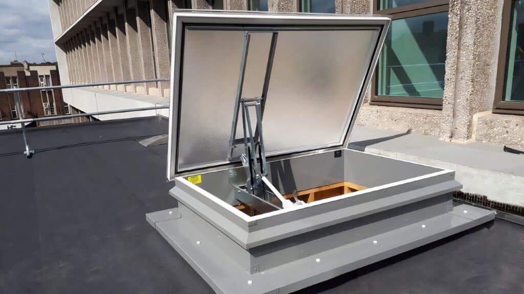 Rooftop access hatch open under clear sky, with adjacent building details visible. Ideal for roof entry solutions and maintenance access.