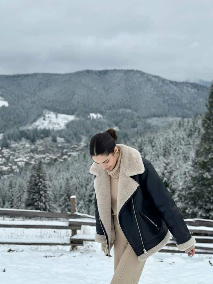 Snow mountains photo shoot idea Person in chic winter outfit against a snowy mountain landscape. Cozy jacket and beige ensemble complement the serene outdoor setting. | Sky Rye Design Person in chic winter outfit against a snowy mountain landscape. Cozy jacket and beige ensemble complement the serene outdoor setting.