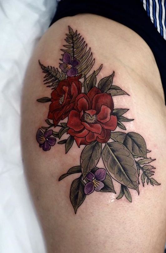 Sophia Baughan flower tattoo Floral thigh tattoo featuring red roses, purple flowers, green leaves, and ferns, showcasing intricate botanical artwork on skin. | Sky Rye Design Floral thigh tattoo featuring red roses, purple flowers, green leaves, and ferns, showcasing intricate botanical artwork on skin.