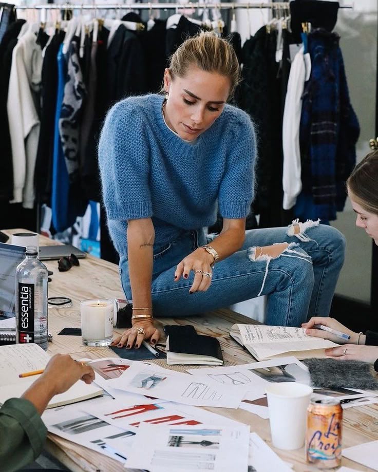 Fashion designer reviewing sketches in studio, surrounded by clothing samples and design drafts on a creative workspace.