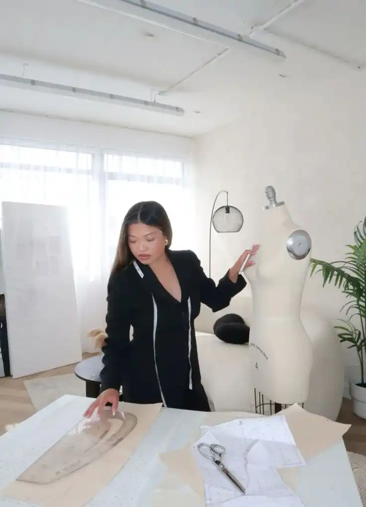 Start your fashion designer journey by learning how to make your own patterns today Fashion designer in a studio working with patterns and a mannequin, wearing a black outfit, creating unique clothing designs. | Sky Rye Design Fashion designer in a studio working with patterns and a mannequin, wearing a black outfit, creating unique clothing designs.