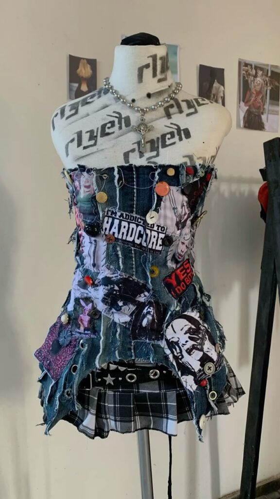 Punk fashion dress with patches and buttons on a mannequin, featuring denim and plaid, emphasizing unique DIY style.