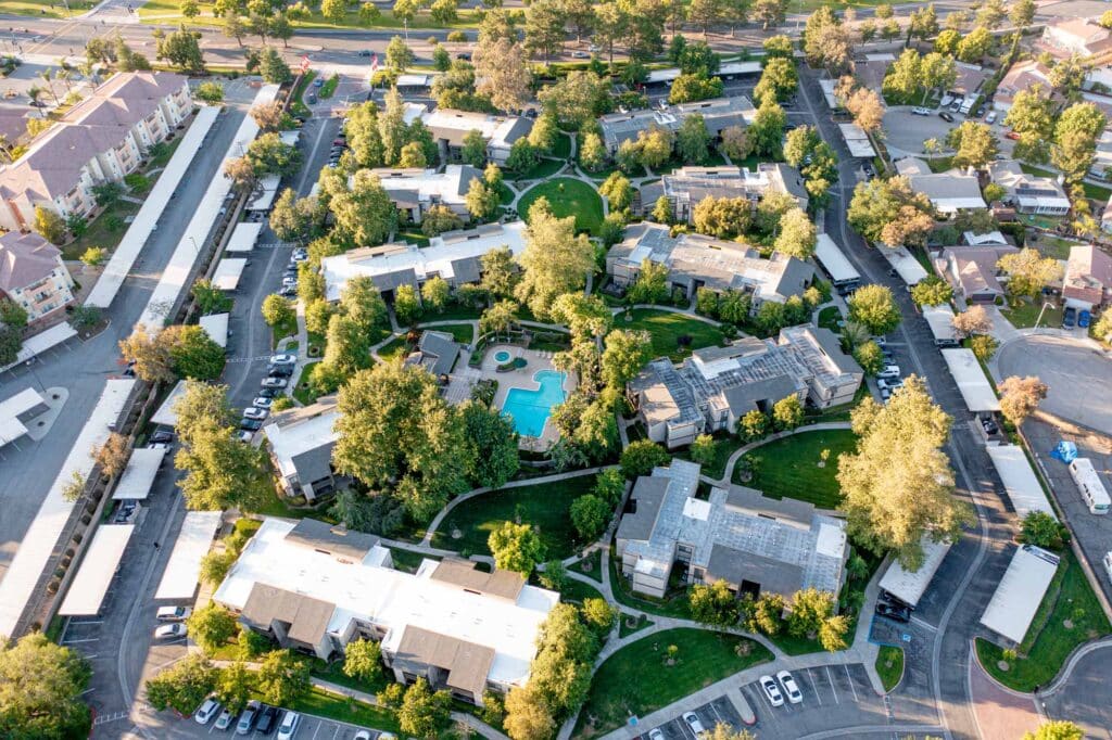 Aerial view of a lush apartment complex featuring a central swimming pool, surrounded by greenery, pathways, and parking spaces.