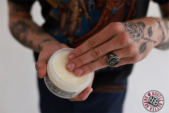 Tattoo Aftercare Guide_ How To Care For Your New Tattoo Tattoo After Tattooed hand applying Hustle Butter to skin, showcasing skincare product use. | Sky Rye Design Tattooed hand applying Hustle Butter to skin, showcasing skincare product use.