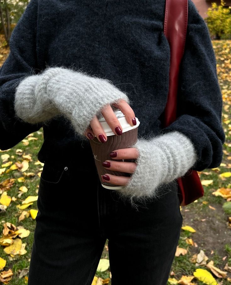 The wrist warmers are back🩶 __cubusofficial Person in cozy sweater with fingerless gloves holds a coffee cup outdoors, surrounded by autumn leaves. | Sky Rye Design Person in cozy sweater with fingerless gloves holds a coffee cup outdoors, surrounded by autumn leaves.