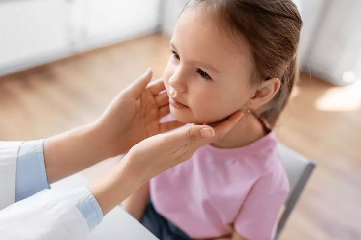 Doctor examining a young girl in a pink shirt during a medical check-up. Child health assessment in a clinic setting.