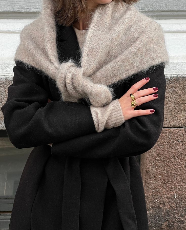 Fashionable woman in black coat and beige scarf, showcasing elegant red nails and a gold ring. Cozy winter style, chic accessories.