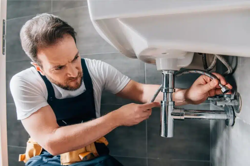 Types-of-Plumbing-Services-You-Need-a-Pro-For-1024x680 Plumber repairing a sink pipe under a bathroom basin. Skilled technician in uniform fixing plumbing issues in a modern setting. | Sky Rye Design Plumber repairing a sink pipe under a bathroom basin. Skilled technician in uniform fixing plumbing issues in a modern setting.