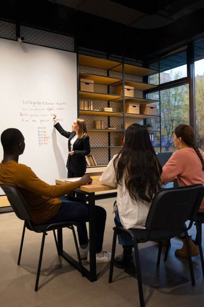 Teacher guides diverse students during Spanish lesson in a modern classroom with a focus on grammar concepts written on the board.