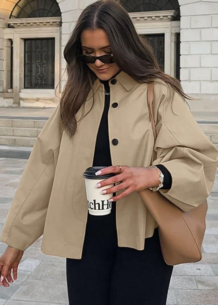 Urban Ease - Cropped Trench Jacket - Beige _ M Stylish woman in beige coat holding coffee, wearing sunglasses, and carrying a brown bag. Fashionable urban outfit in a city setting. | Sky Rye Design Stylish woman in beige coat holding coffee, wearing sunglasses, and carrying a brown bag. Fashionable urban outfit in a city setting.