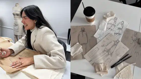 A fashion designer joyfully sketches on fabric, with garment designs and fabrics displayed on a nearby table with a coffee cup.