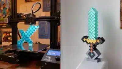 3D printer creating a pixelated sword, inspired by video games, with a completed sword displayed next to it on a stand.