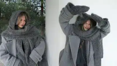 Woman in oversized gray coat and scarf outdoors, posing playfully in cozy winter attire.