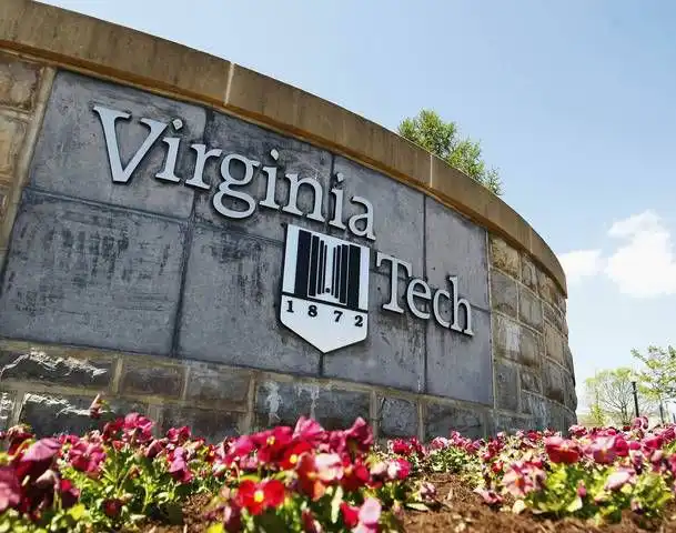 Virginia Tech sign with vibrant flowers in foreground under a clear blue sky, highlighting the campus entrance.
