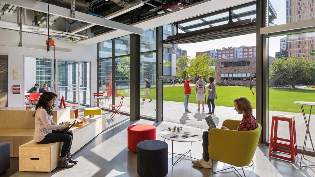 WIT-Center-Engineering-Innovation-Sciences-Acentech-interior-03-lr Modern open office space with people working inside and chatting outside in a sunny green courtyard. Collaborative and relaxed atmosphere. | Sky Rye Design Modern open office space with people working inside and chatting outside in a sunny green courtyard. Collaborative and relaxed atmosphere.