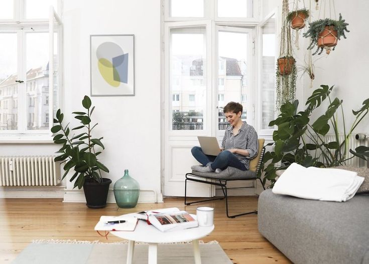 Want your home to feel more adult_ Heres the interior investment to make in every room thatll get you there Well+Good Woman working on a laptop in a bright, minimalist living room with plants and large windows, creating a serene and cozy atmosphere. | Sky Rye Design Woman working on a laptop in a bright, minimalist living room with plants and large windows, creating a serene and cozy atmosphere.