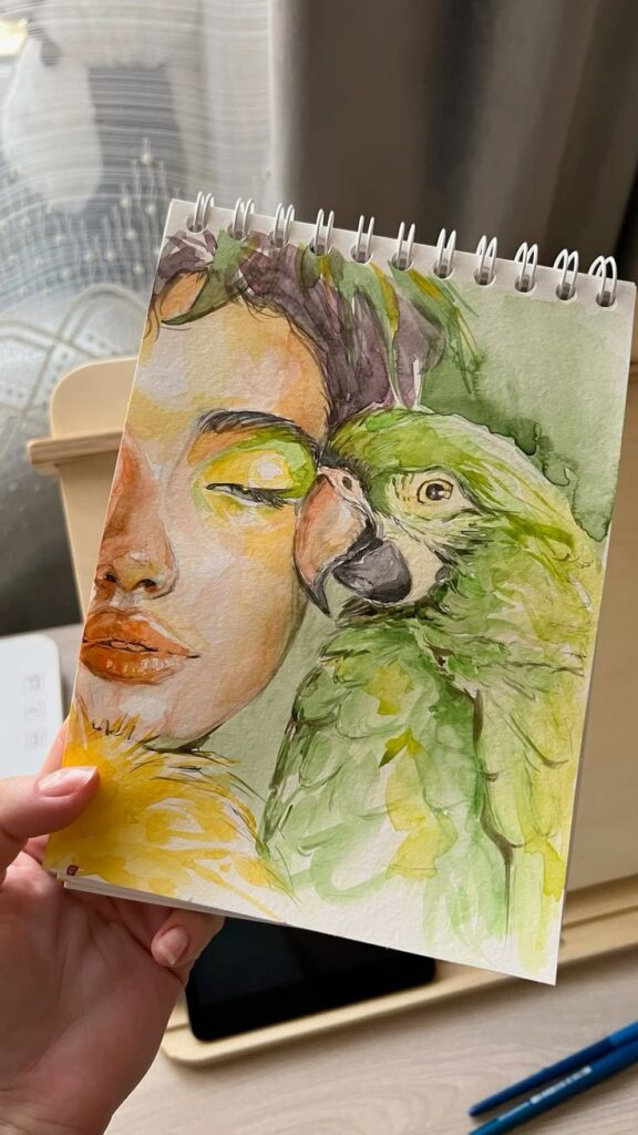 Watercolor art of a woman and green parrot on a sketchbook, showcasing vibrant yellow and green hues.