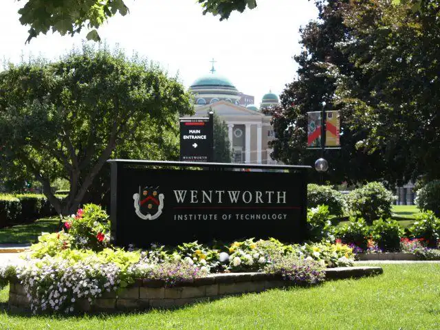 Entrance sign of Wentworth Institute of Technology surrounded by lush greenery and flowers on a sunny day.