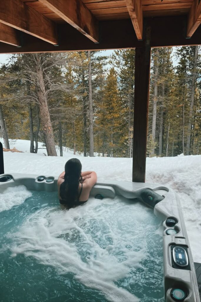 Person relaxing in a hot tub overlooking a snowy forest, under a wooden deck. Cozy winter retreat and relaxation concept.