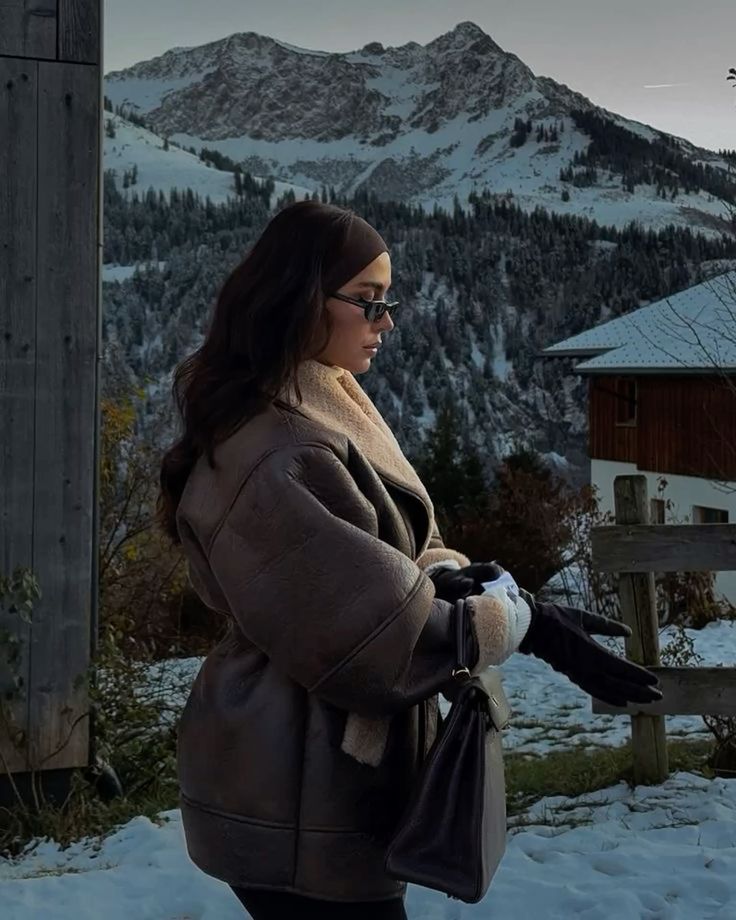 Winter aesthetic outfits 2026 _ зимняя эстетика и образы Woman in winter coat and gloves stands in snowy mountain village, surrounded by rustic wooden buildings and snow-capped peaks. | Sky Rye Design Woman in winter coat and gloves stands in snowy mountain village, surrounded by rustic wooden buildings and snow-capped peaks. Winter Photography Workshops