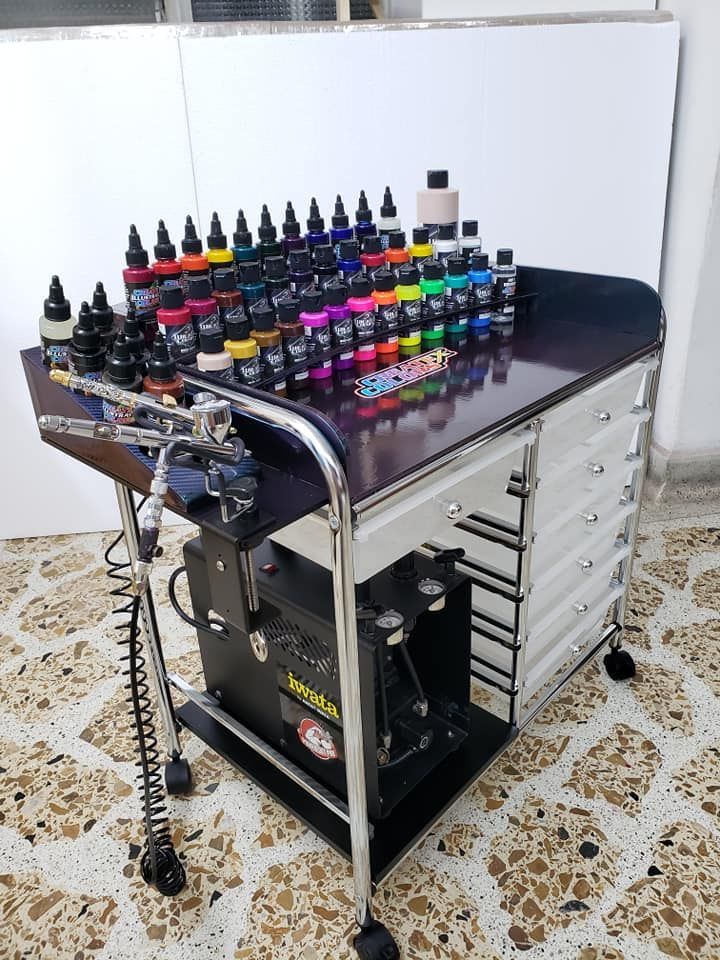 Work Station Tattoo inks and equipment on a wheeled cart, showcasing diverse colors for vibrant tattoo designs, placed on a patterned floor. | Sky Rye Design Tattoo inks and equipment on a wheeled cart, showcasing diverse colors for vibrant tattoo designs, placed on a patterned floor.