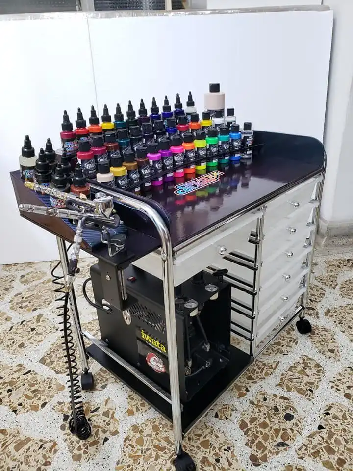 Tattoo inks and equipment on a wheeled cart, showcasing diverse colors for vibrant tattoo designs, placed on a patterned floor.